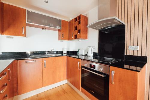 uma cozinha com armários de madeira e electrodomésticos pretos em Leeds City Centre Dock 2 Bed 2 Bath em Hunslet