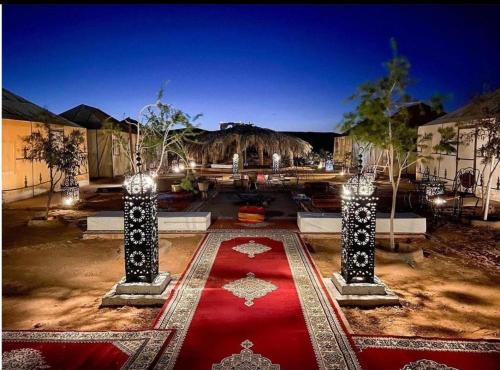 a courtyard with a red carpet and two columns with lights at Sandrela Luxury Camp in Merzouga