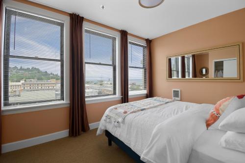 a bedroom with two windows and a bed and a mirror at Norblad Hotel in Astoria, Oregon