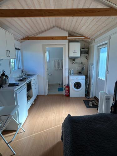 a room with a bed and a kitchen with a washing machine at Hlíðarás Guesthouse in Ölfus