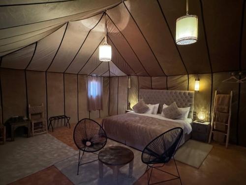 a bedroom in a tent with a bed and two chairs at Erg Chebbi Sahara Camp in Merzouga