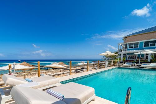 a swimming pool with chairs and umbrellas and the ocean at Cobalt Coast Resort in West Bay