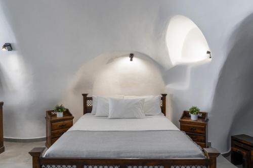 1 dormitorio con 1 cama con pared blanca en Enalion Suites, en Oia