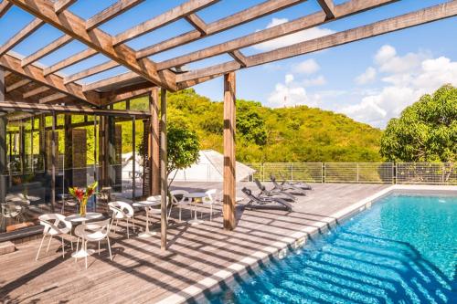 an outdoor deck with a pool and a wooden pergola at Villa Noucinq in Le Gosier