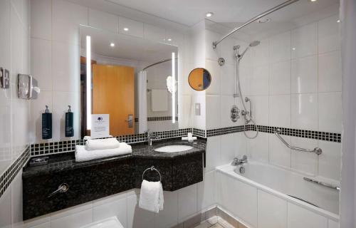 a bathroom with a sink and a tub and a mirror at DoubleTree by Hilton Swindon Hotel in Swindon