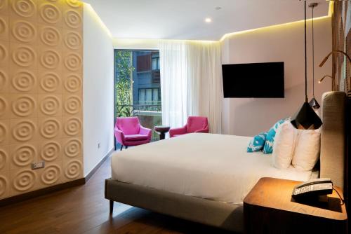a hotel room with a bed and chairs and a window at The Fives Downtown Hotel & Residences, Curio Collection by Hilton in Playa del Carmen