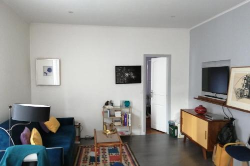 Apartment at the gateway to Paris في فينسين: غرفة معيشة مع أريكة زرقاء وتلفزيون