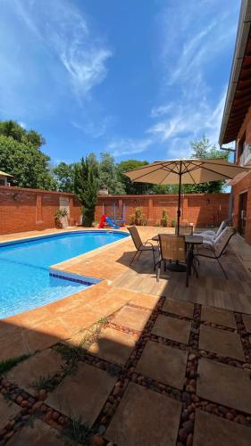 eine Terrasse mit einem Tisch und einem Sonnenschirm neben einem Pool in der Unterkunft Casa Hotel Confortable in Encarnación