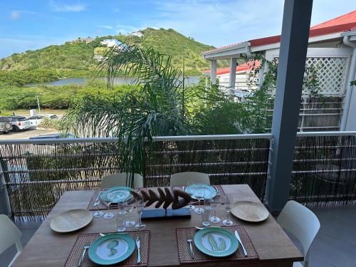 a wooden table with plates and wine glasses on a balcony at Appartement Saint Martin Friars Bay Sunset Paradise in Friar's Bay