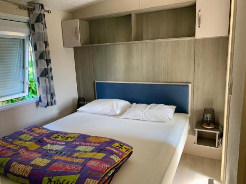 a small bedroom with a bed with a blue headboard at Mobile home Cc780 Siblu Les Charmettes close to the sea in Les Mathes