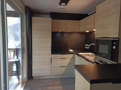 eine Küche mit Holzschränken und einem großen Fenster in der Unterkunft Chalet 2 Chambres à Labouheyre avec Piscine Chauffée, WiFi et Terrasse au Bord d'un Lac - FR-1-783-25 in Labouheyre