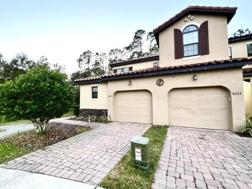 a house with two garage doors and a brick driveway at Cozy Family Town Home Close to Disney townhouse in Kissimmee
