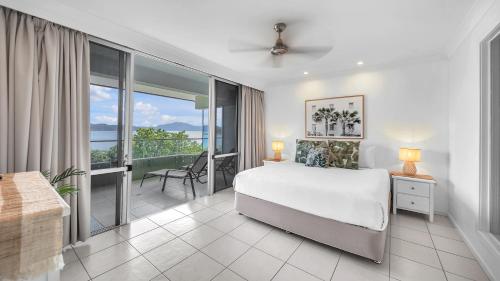 a white bedroom with a bed and a balcony at Lagoon Beachfront Lodge 206 on Hamilton Island by HamoRent in Hamilton Island