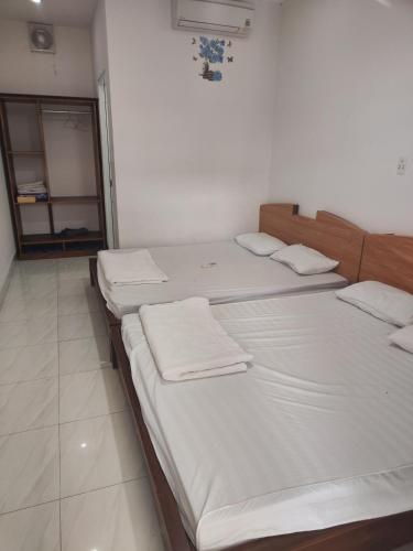 Habitación con 4 camas, sábanas blancas y espejo. en NHÀ NGHỈ PHÚ QUÝ, en Ho Tram