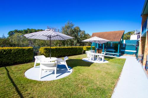 a patio with two white chairs and an umbrella at Tannum On The Beach Motel in Tannum Sands