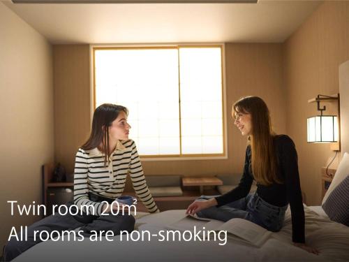 two girls sitting on a bed in a room at Hotel Resol Kyoto Shijo Muromachi in Kyoto