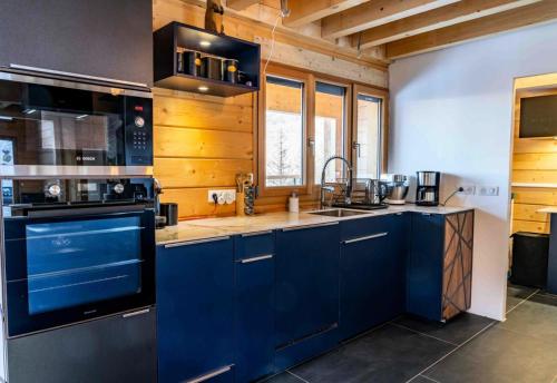 La cuisine est équipée de placards bleus et d'un four avec plaques de cuisson. dans l'établissement Résidence Pramouton - Chalet moderne avec vue splendide sur la vallée MAE-0401, à Le Mélézet