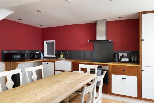 a kitchen with a wooden table and red walls at Stag Cottage, Sea wall in Whitstable