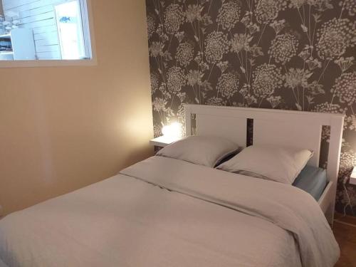 1 cama blanca en un dormitorio con papel pintado con motivos florales en La Cabane du Roc, en Granville