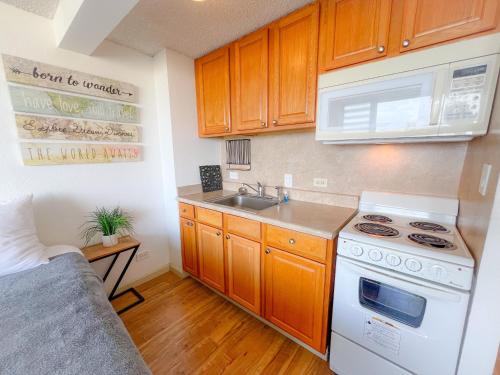 Il comprend une petite cuisine équipée d'une cuisinière et d'un évier. dans l'établissement Bright Waikiki Studio condo, à Honolulu