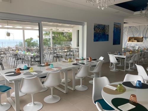 un ristorante con tavoli bianchi, sedie e finestre bianche di Camping La Scogliera - Maeva Vacansoleil a Castro di Lecce