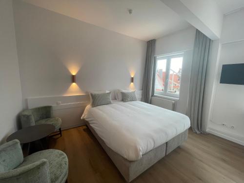 Strandhotel De Haan في دي هان: غرفة نوم بسرير ابيض كبير وكرسيين