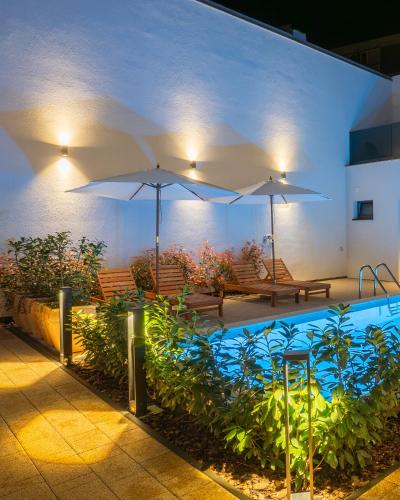 a swimming pool with two umbrellas and two benches at Goldberg Apartments Osijek in Osijek