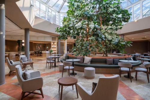 una hall con tavoli, sedie e un grande albero di Hilton Garden Inn Bologna North a Bologna