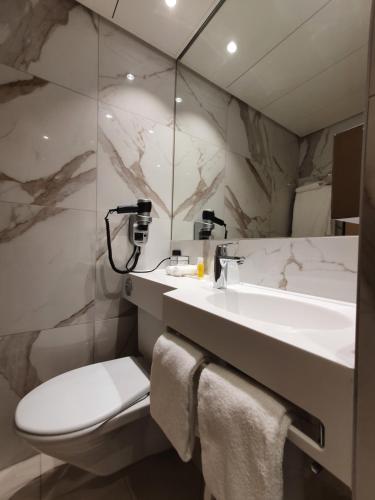 uma casa de banho com um lavatório, um WC e um espelho. em Nash Airport Hotel em Genebra