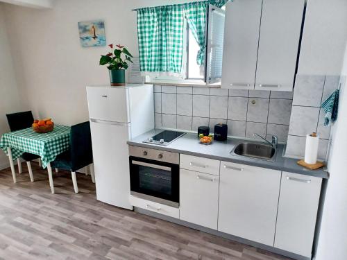 a kitchen with white cabinets and a sink and a table at Apartmani Leženić Dada in Neum