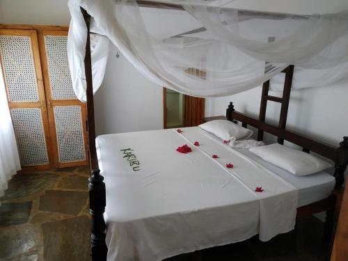 Silver Rock Hotel في ماليندي: سرير عليه شراشف بيضاء وورود حمراء