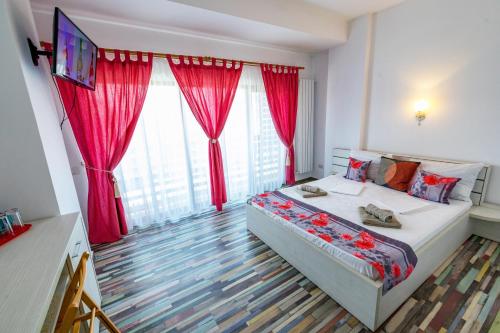 a bedroom with a bed with red curtains and a television at Casa Amelie Mangalia in Mangalia