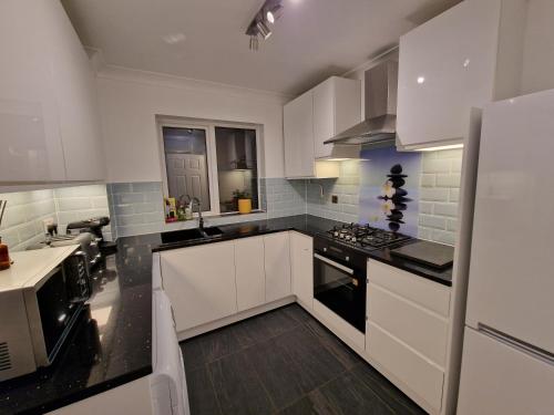 a kitchen with white cabinets and black counter tops at Modern And Spacious 3 Bedroom Family House with Workspace in Colchester