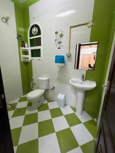 a green and white bathroom with a toilet and sink at Orchid sur guest house in Sur