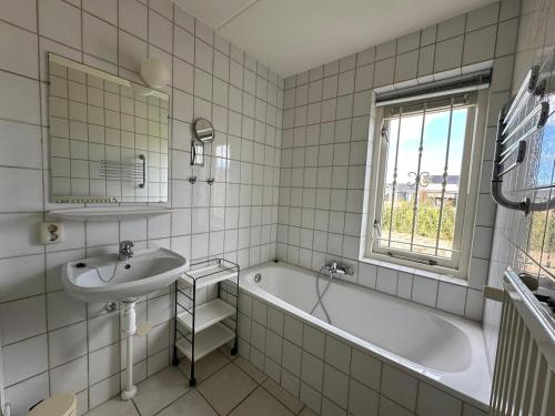 een wit betegelde badkamer met een wastafel en een bad bij Crox Houcke 59 in Nieuwvliet