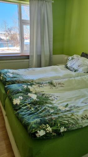 a bed with a floral blanket on it with a window at Fornilækur Guesthouse in Blönduós