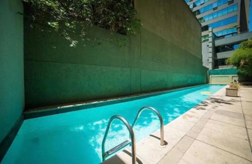 Luminosa habitacion con baño privado en el centro de Providencia في سانتياغو: مسبح ازرق بجدار اخضر ودرج