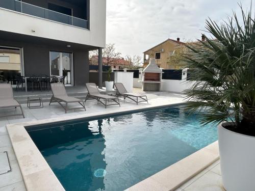 a swimming pool with lounge chairs next to a house at Apartments Cesare in Nin