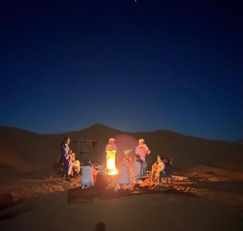 a group of people around a bonfire in the desert at Sahara Tours luxury camp in Merzouga