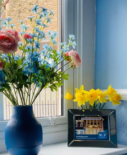 a blue vase with flowers and a clock next to a window at All Seasons Bed & Breakfast - Adults Only in Weston-super-Mare