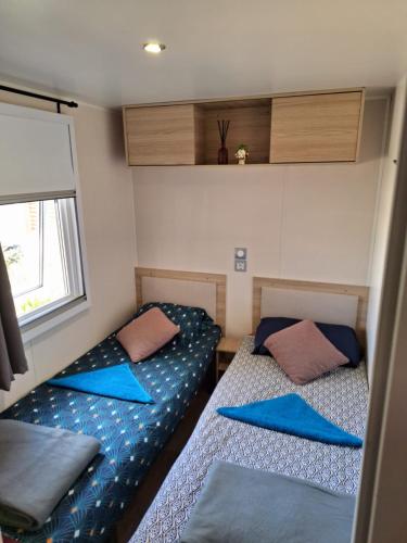 - 2 lits dans une petite chambre avec des oreillers bleus dans l'établissement Mobil-home camping Mar Estang, à Canet