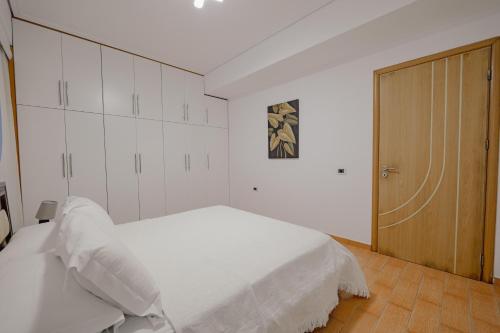 a bedroom with a white bed and a wooden door at Villa Xika in Sarandë
