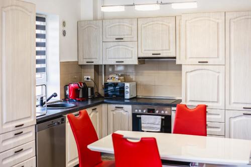 a kitchen with white cabinets and a table and red chairs at Leon's home in Şelimbăr