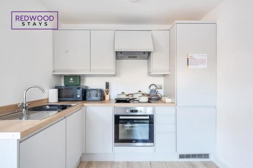 a white kitchen with white cabinets and a sink at Modern Serviced Apartments For Contractors & Families with Free Parking, WiFi & Netflix By Redwood Stays in Basingstoke