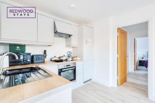 una cocina con armarios blancos y un cartel que lee estancias renovadas en Modern Serviced Apartments For Contractors & Families With FREE Parking, WiFi & Netflix By REDWOOD STAYS, en Basingstoke