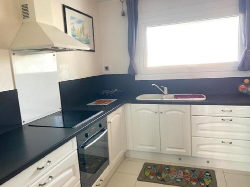 une cuisine avec des armoires blanches, un évier et une fenêtre dans l'établissement Appartement avec piscine roof top, à Saint-Gilles-Croix-de-Vie