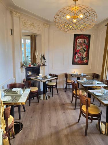 uma sala de jantar com mesas e cadeiras e um lustre em Le Castel Guesthouse em Bayeux