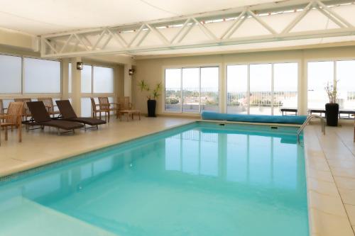 une grande piscine avec des chaises, des tables et des fenêtres dans l'établissement Résidence Maricel, à Canet