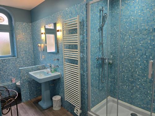 a blue tiled bathroom with a sink and a shower at Le Castel Guesthouse in Bayeux