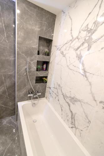 La salle de bains est pourvue d'une baignoire blanche et d'un mur en marbre. dans l'établissement Appartement spacieux proche du centre-ville de Villeurbanne, à Villeurbanne